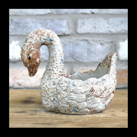 Decorative swan planter on a wooden surface with a stone wall background